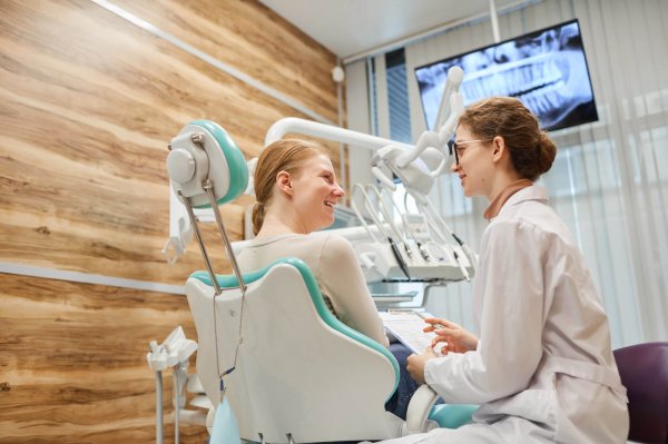 Young woman sitting on dental chair and consulting with dentist during her visit at dental clinic